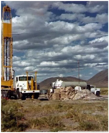 Truck-mounted drill rig at a geothermal well site, with stacked supply bags and a water truck